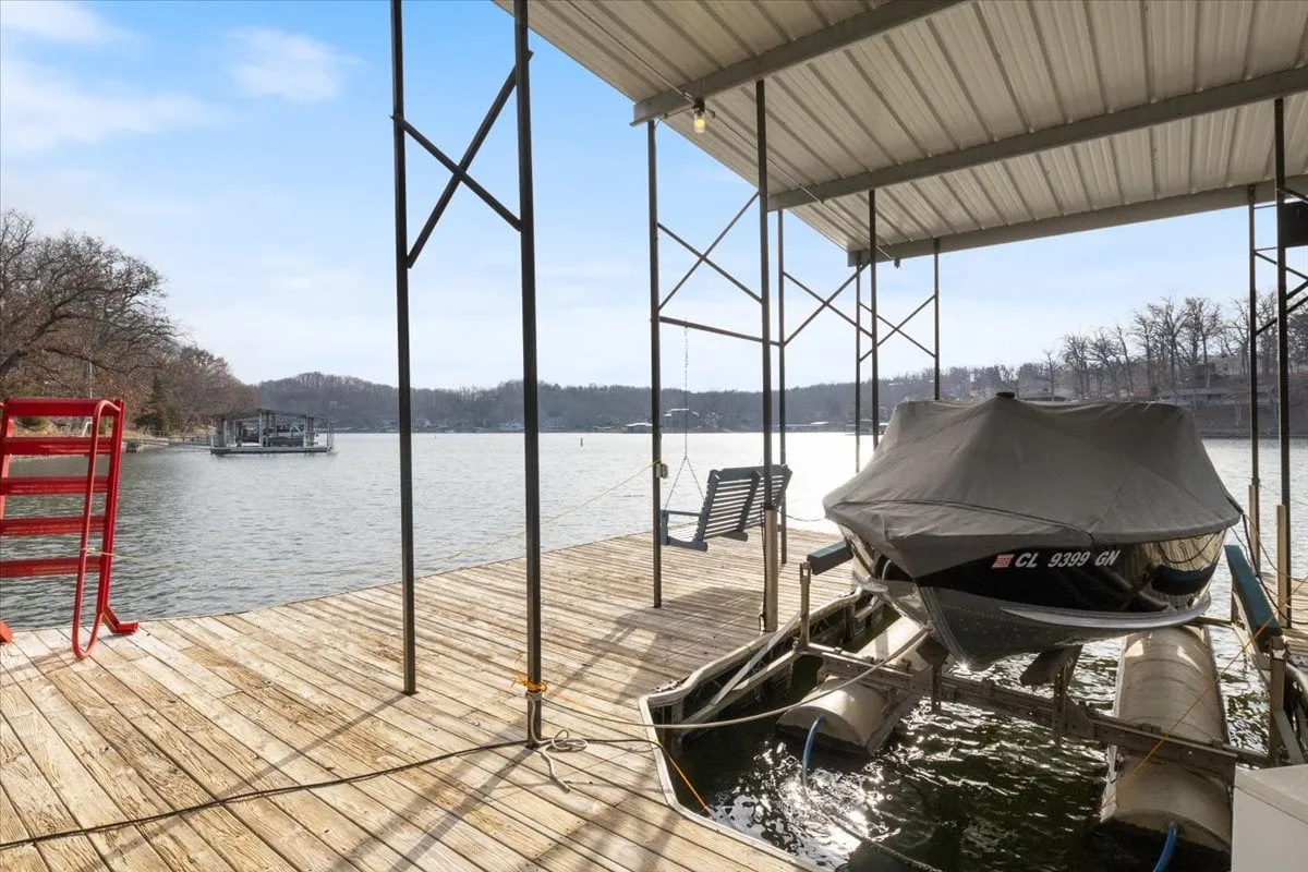 A private dock stretches out onto the sparkling lake, with a boat tied up and surrounded by leafy trees. The dock invites boating excursions, fishing, or simply relaxing by the water, offering a key amenity for those looking to explore Lake of the Ozarks.