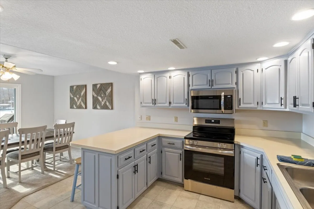 This image features a welcoming kitchen with a central island, stainless steel appliances, and light blue cabinetry. In the background, a dining area is visible, tying together the kitchen and dining spaces. The scene conveys warmth and sociability, with clear areas for cooking, gathering, and sharing meals.