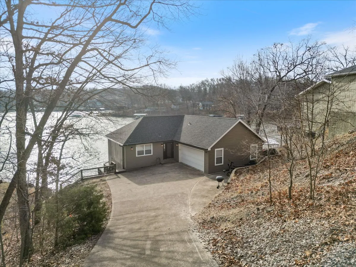 This exterior image captures the house with its driveway, surrounded by trees and featuring a sweeping view of the adjacent lake. It hints at both the convenience of access and the scenic, natural setting, highlighting the easy transition from home to lakeside adventures.