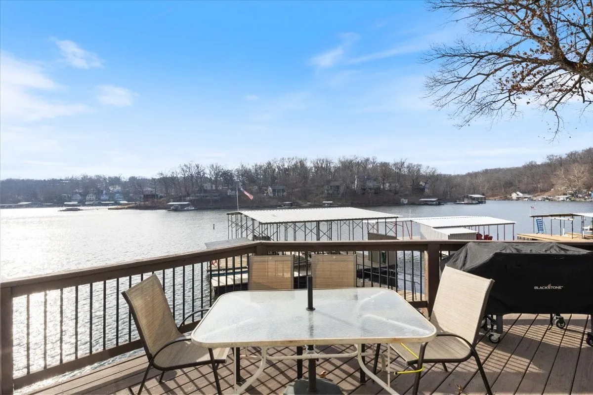 An exterior shot featuring an outdoor dining table and grill on a deck overlooking the lake and dock below. The view highlights how the living space seamlessly transitions outdoors, with inviting spots for al fresco meals and gatherings while enjoying the lake view.