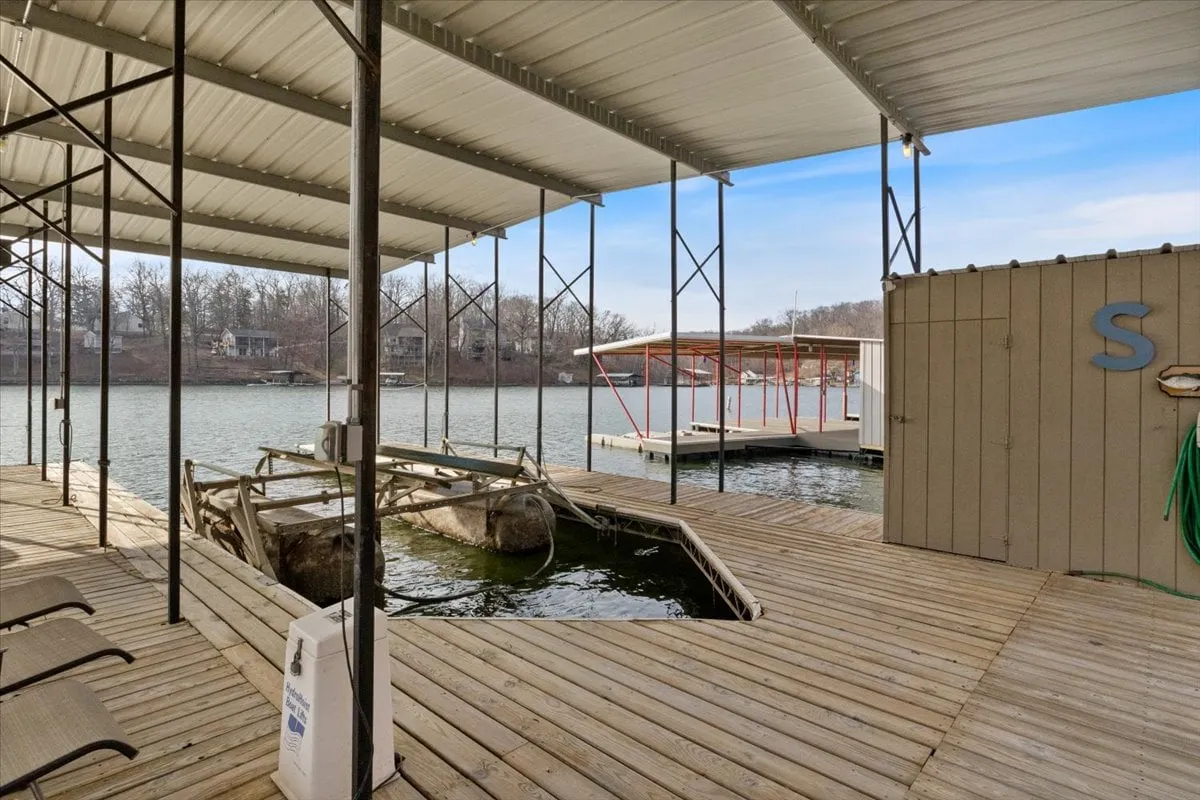 This exterior image captures the dock area extending into the calm lake, with tranquil water and the surrounding landscape visible. The dock is clearly set up for boating and fishing, and the peaceful mood is accentuated by the soft lighting, suggesting either morning or evening. It visually represents immediate lake access and direct interaction with the water.