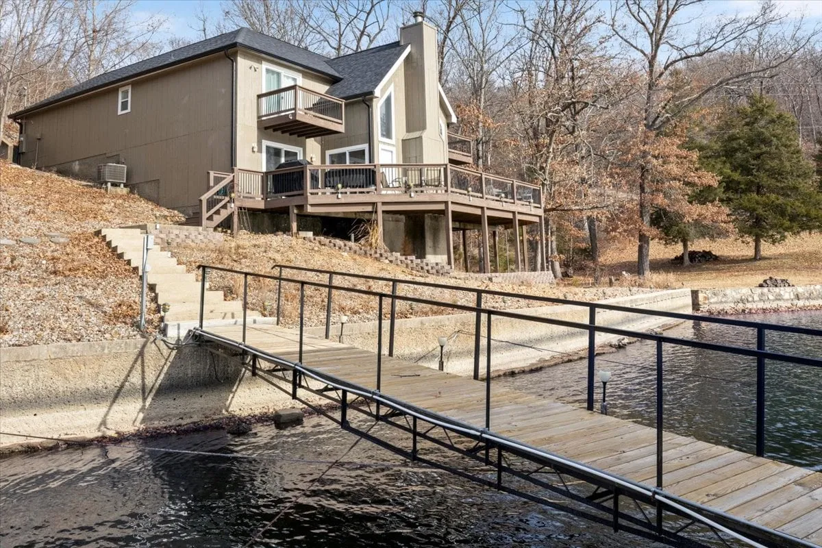 A wide-angle exterior shot capturing the house, wooden dock, shimmering lake, and surrounding trees. The image showcases the property’s seclusion, connection to the water, and natural beauty—establishing a sense of place for guests arriving for a weekend or planning an extended stay.
