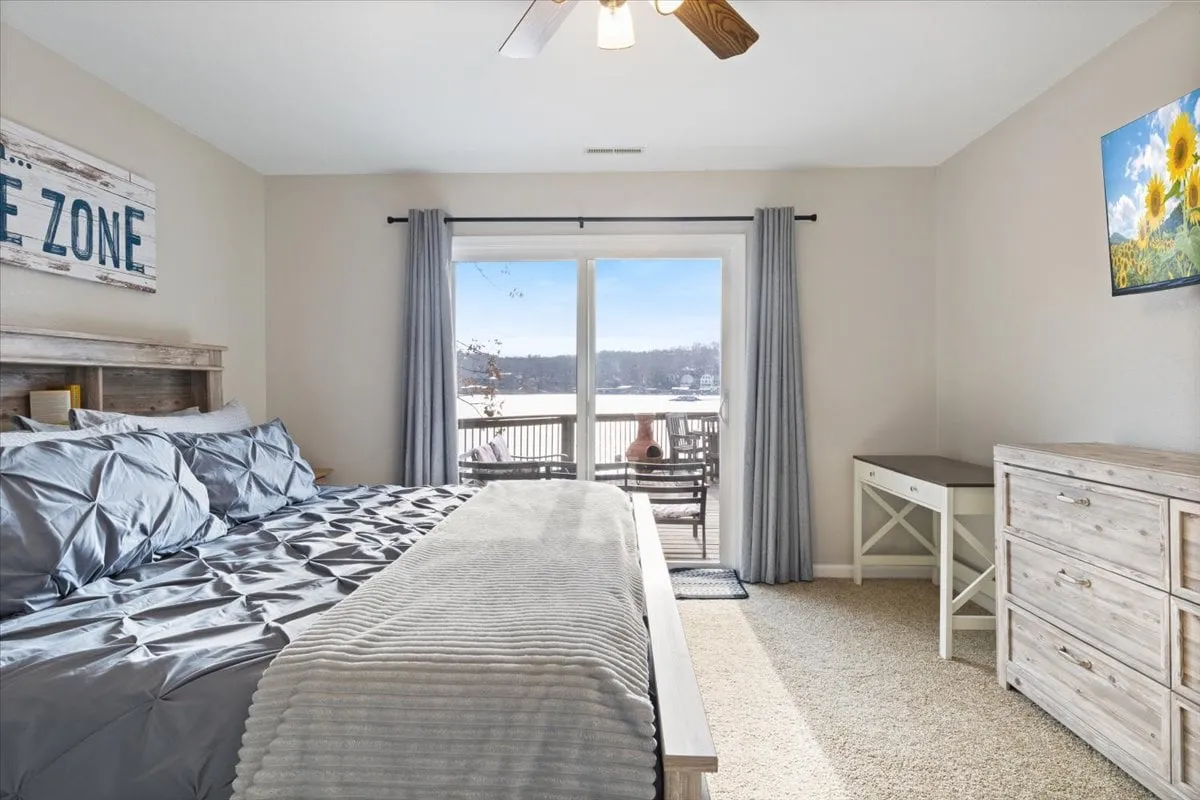 A calm and inviting bedroom with a comfortable bed overlooking a view through sliding doors, a practical dresser, and tasteful artwork. The sliding doors open directly to a balcony or deck, seamlessly connecting the restful indoor space with the fresh air and nature outside.