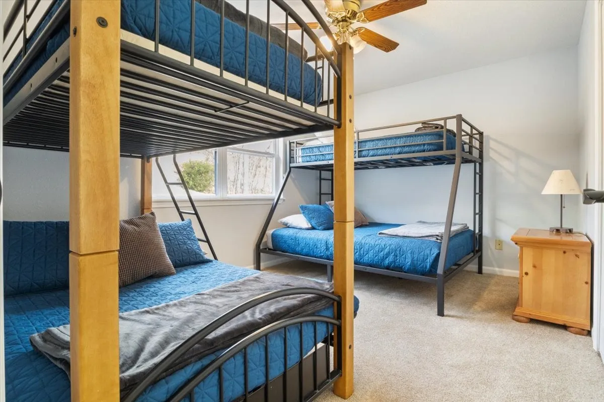 A playful and comfortable bedroom with bunk beds, a bedside table, and windows letting in natural light. This space is inviting for families or children, offering both a sense of togetherness and individual retreat.